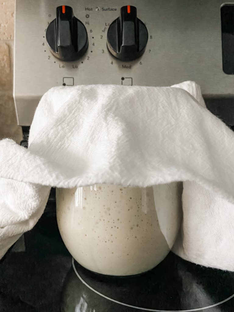 jar with starter covered by white towel on stove top