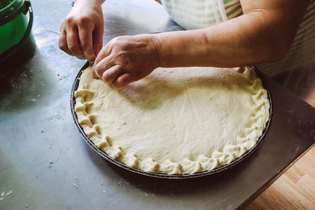 Person Pinching Round Pie Dough on Grey Tray