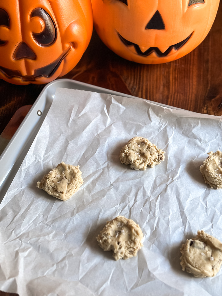 cookie dough on a parchment lined pan next to halloween candy buckets