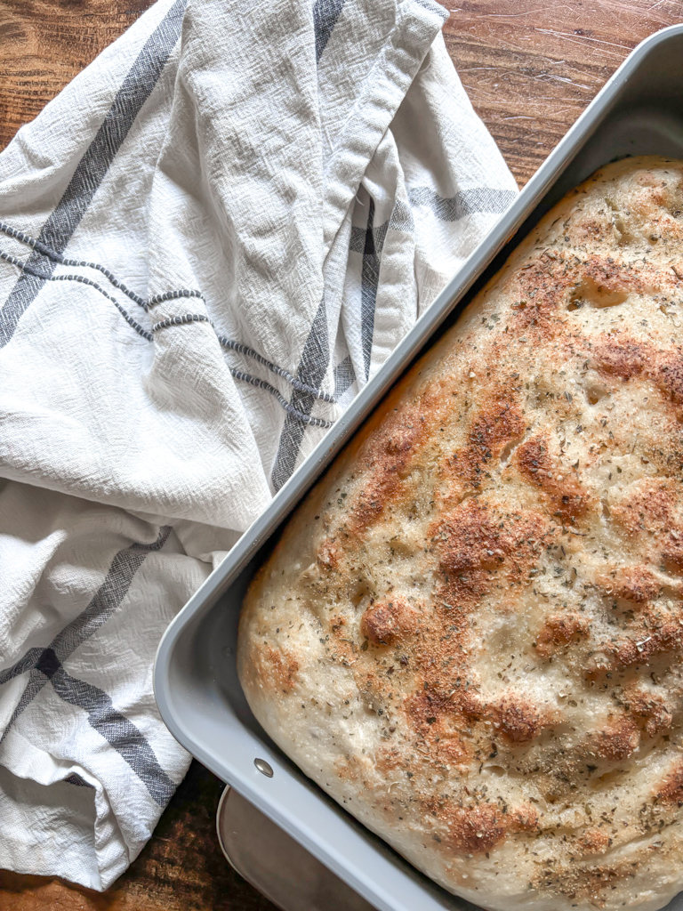 baked fociaccia loaf in a metal pan on top of hand towel