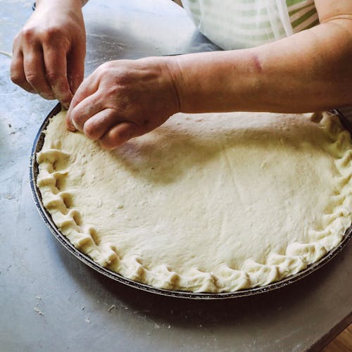 Person Pinching Round Pie Dough on Grey Tray