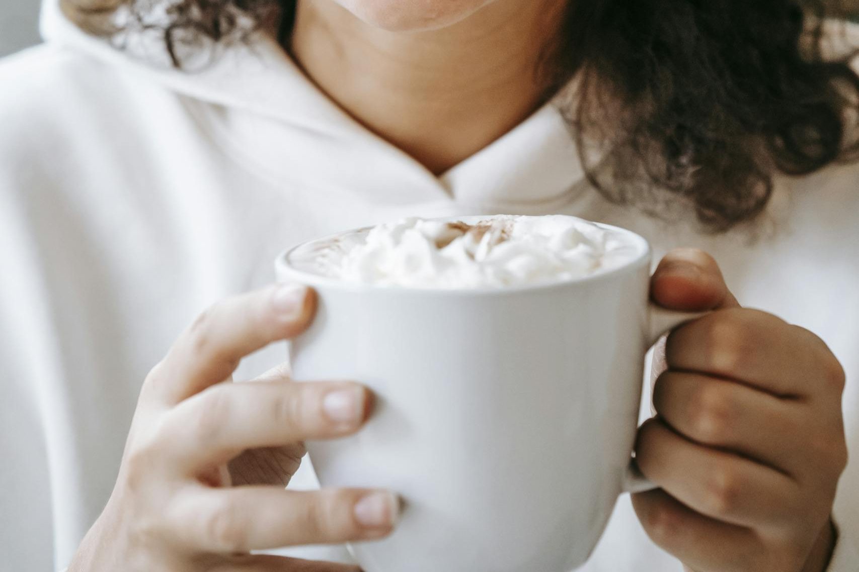 Smiling woman with curly hair savoring a delightful coffee moment indoors.