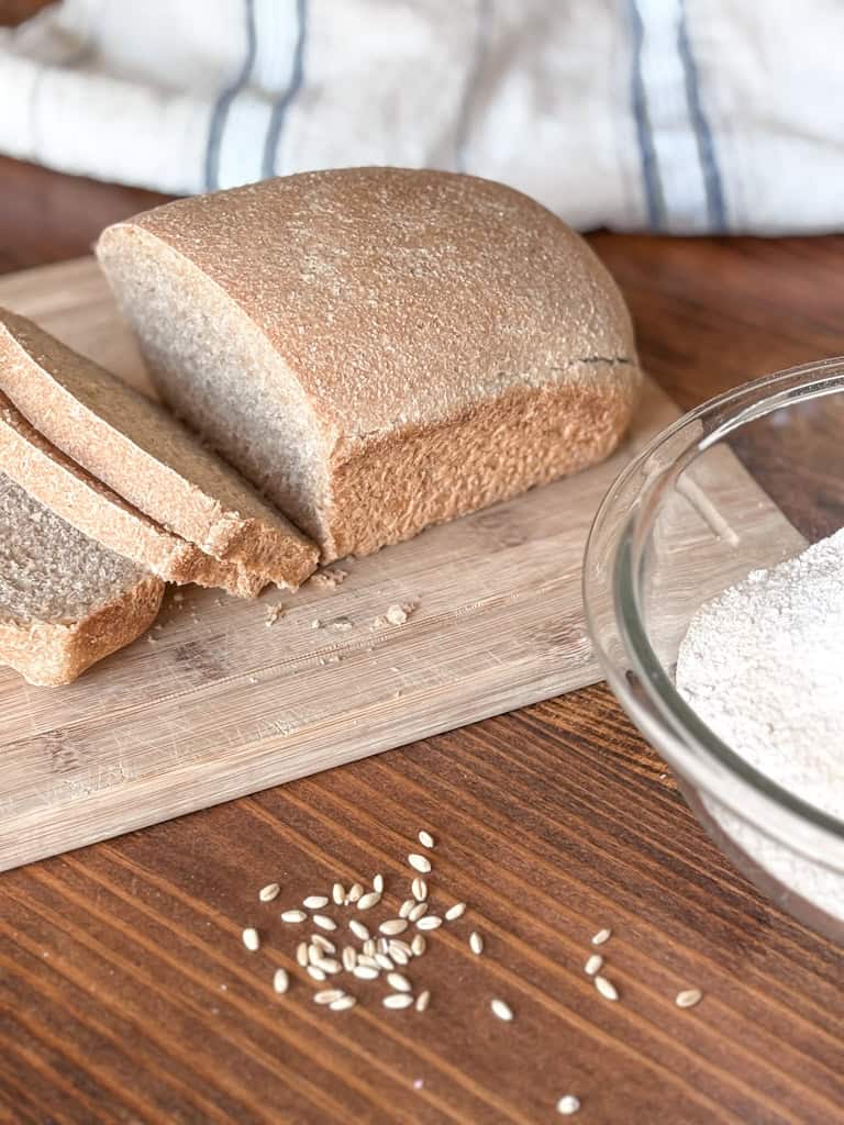 sliced loaf of freshly milled sourdough sandwich bread with a bowl of flour