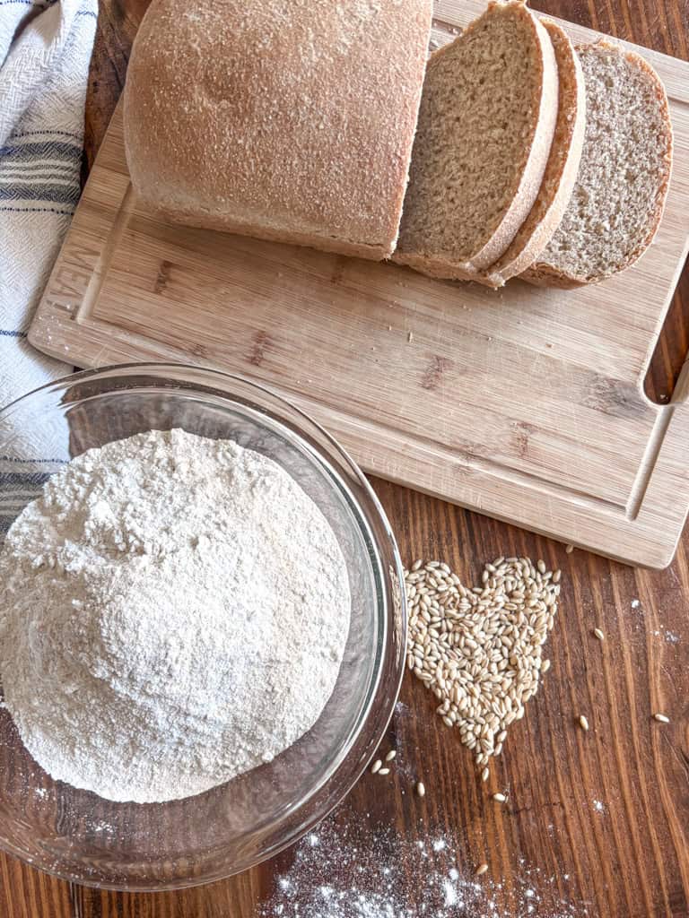  freshly milled sourdough sandwich bread with a bowl of flour and a heart shaped out of wheat berries