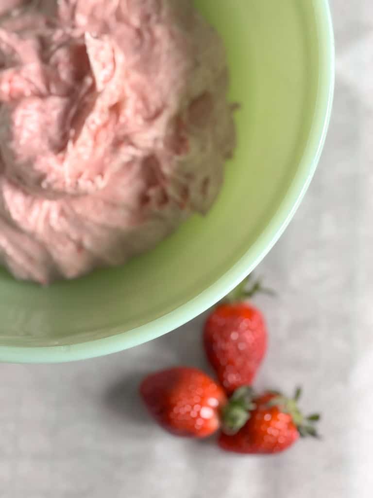 green bowl with strawberry frosing and fresh strawberries nearby