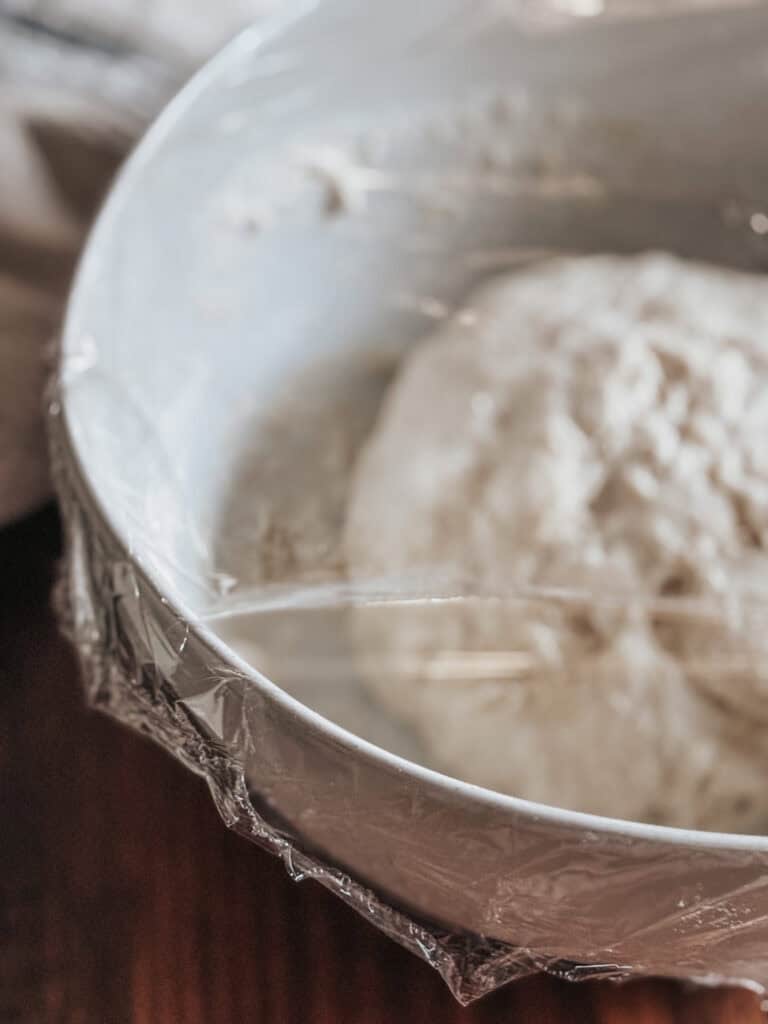 bowl of pizza dough covered with plastic wrap