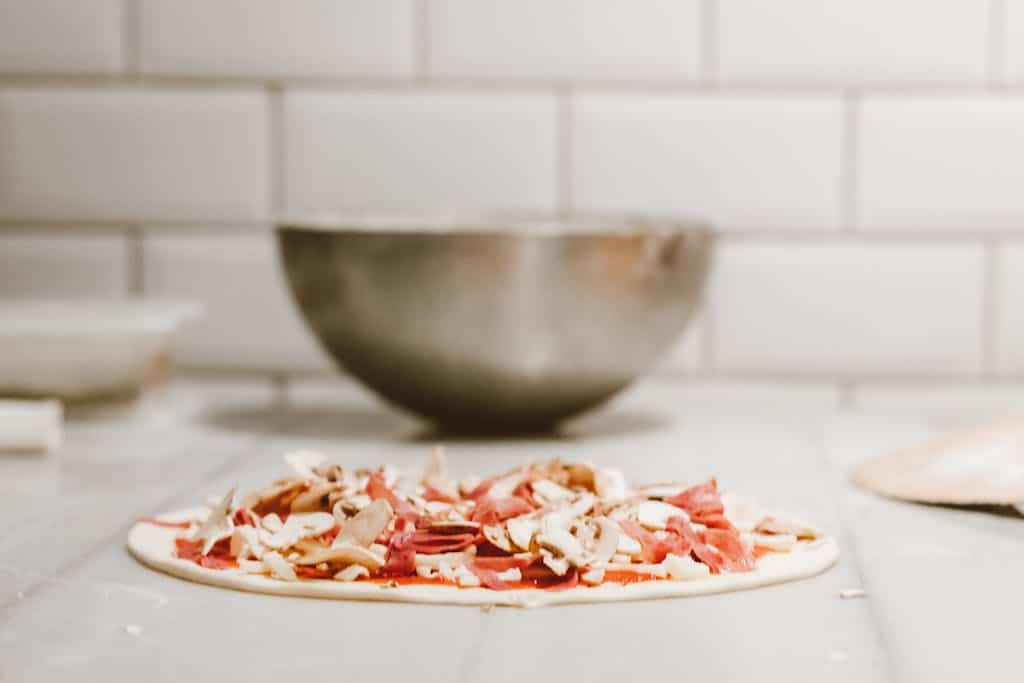 Close-up of homemade pizza dough topped with fresh mushrooms and salami, ready to bake.