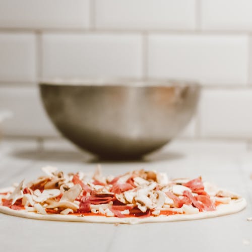 Close-up of homemade pizza dough topped with fresh mushrooms and salami, ready to bake.