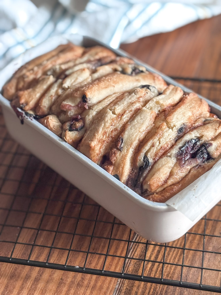 baked sourdough blueberry loaf in a pan on a cooling rack