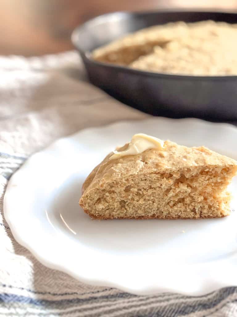 slice of sourdough cornbread on a plate with cast iron skillet of cornbread in the background