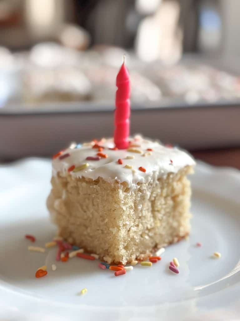 close up of a slice of birthday cake with sprinkles and a pink candle on top.