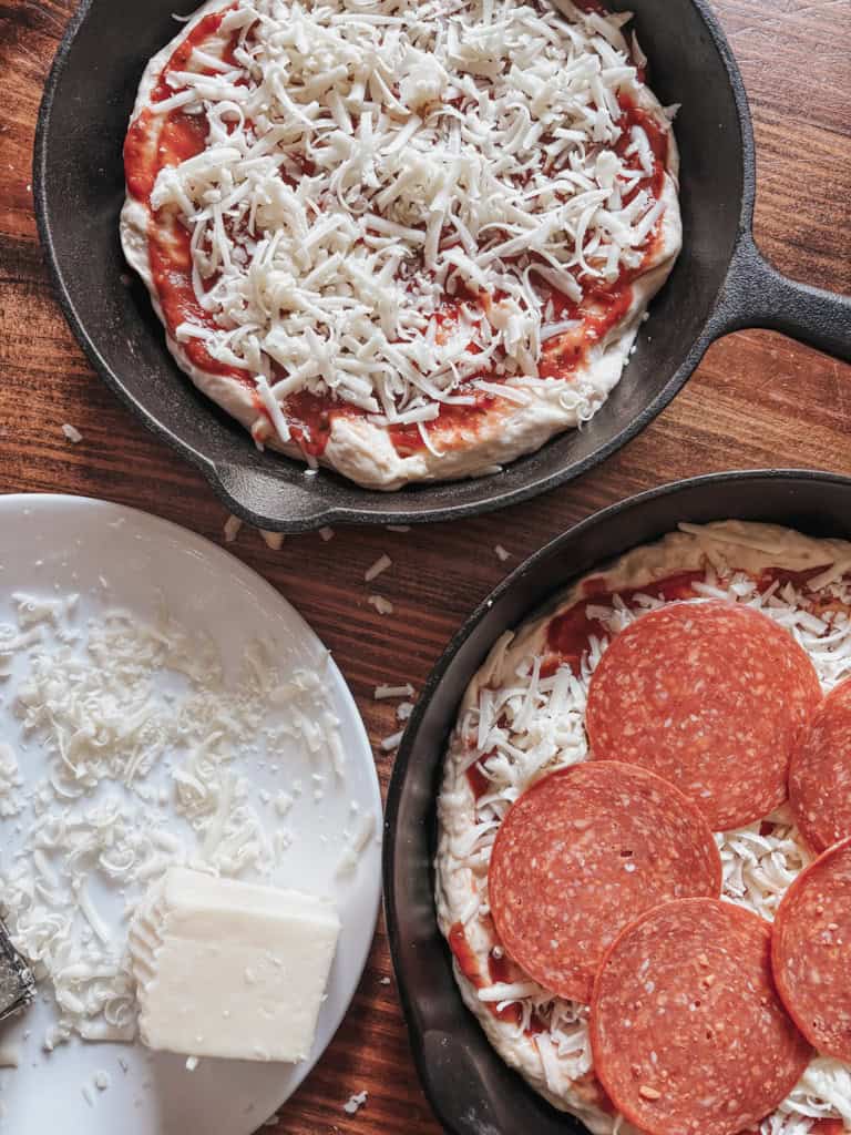 cast iron skillet with unbaked pizza beside a plate of freshly grated cheese