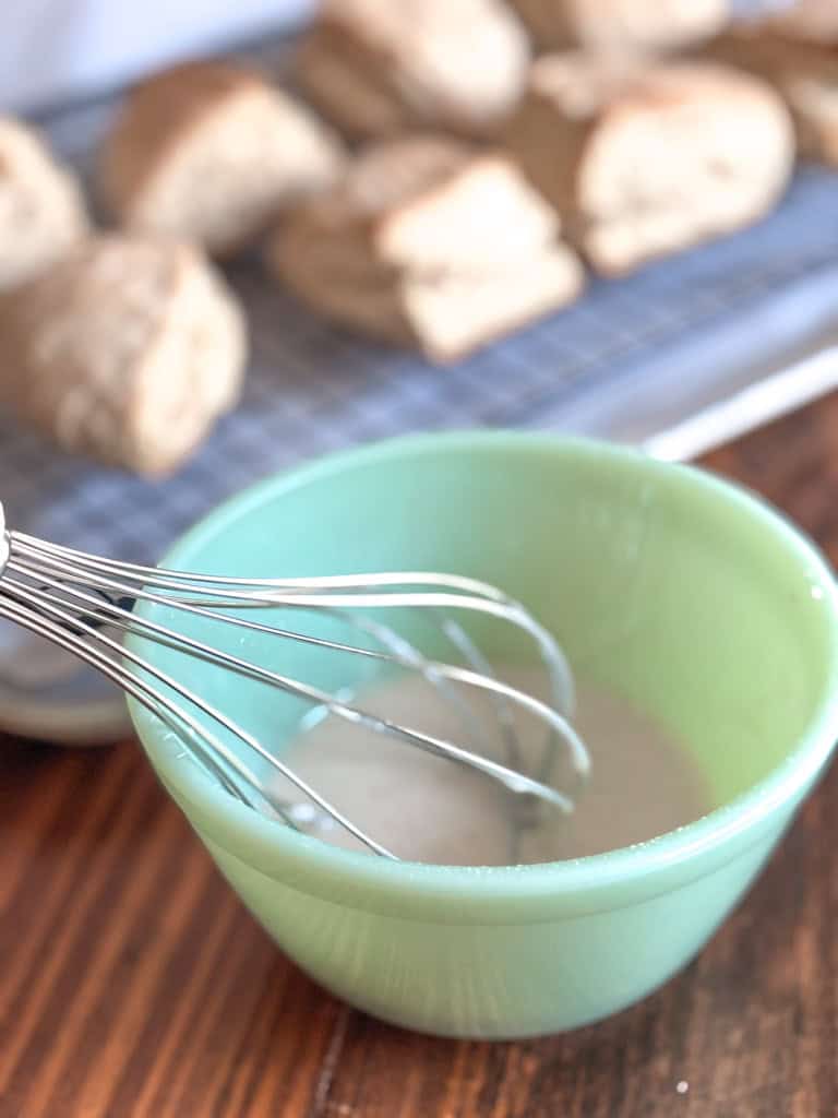 green bowl of cinnamon sugar glaze with whisk inside bowl
