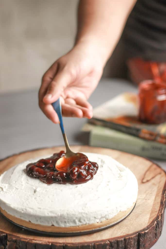 hand spooning jam onto a simple one layer cake on a wooden cake stand