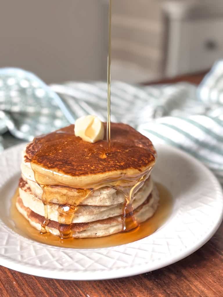 syrup being poured onto a stack of pancakes
