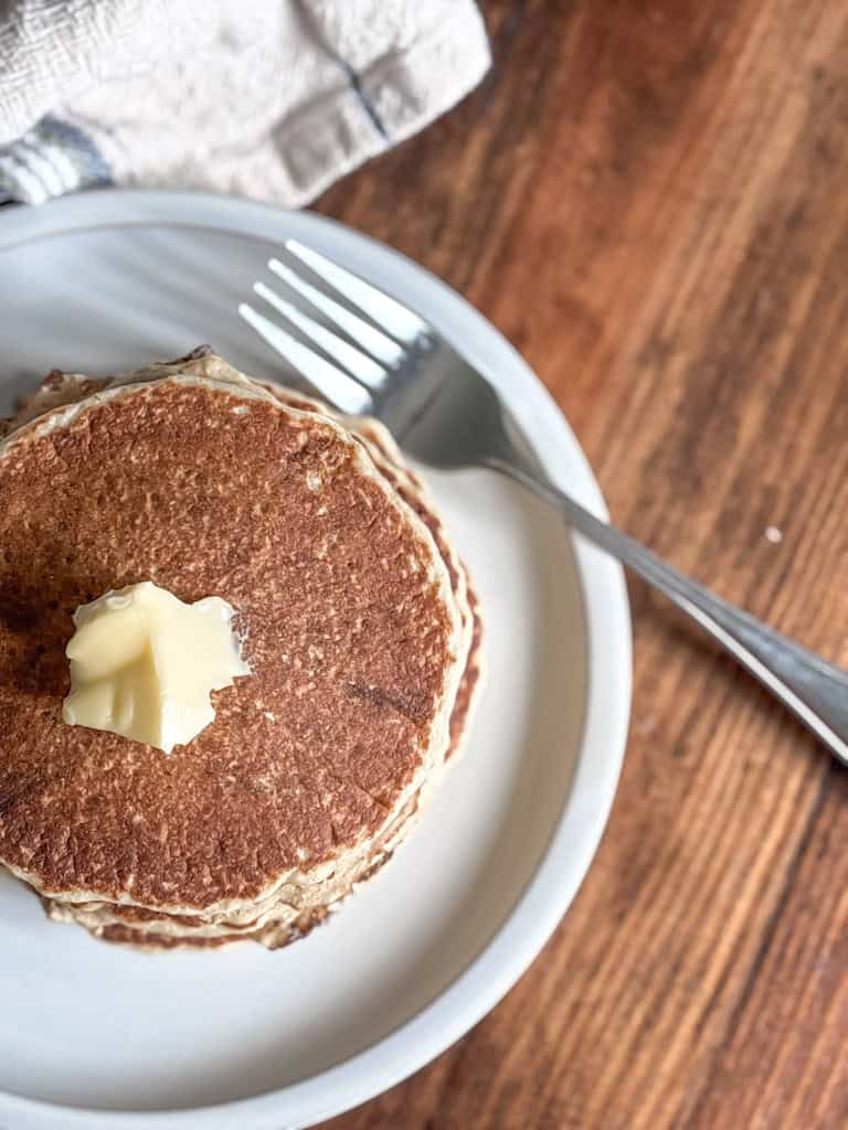 Stack of whole wheat pancakes on a plate with a dollop of butter on top.